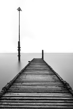 Fototapeta Old abandoned rotted jetty leading out to sea with old fashioned lamppost. 
