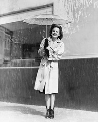 Young woman in a raincoat and umbrella standing in the rain 