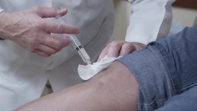 Tight shot of doctor making injection to patient's knee.