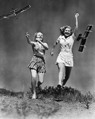 Two women running and playing with model airplanes  - obrazy, fototapety, plakaty