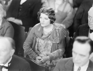 Woman sitting in a auditorium listening with folded hands 