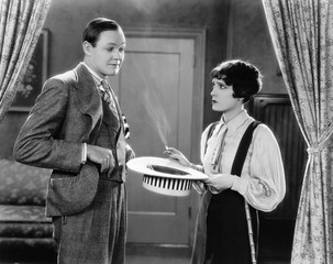 Woman holding hat and smoking interacting with man 