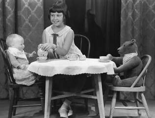 Girl having tea party with doll and bear 