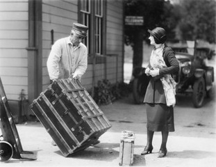 Woman and a porter carrying her trunk 