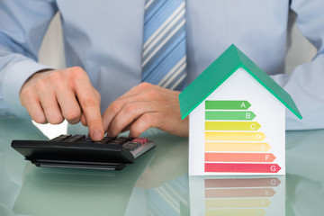 Businessman Using Calculator Near House Model