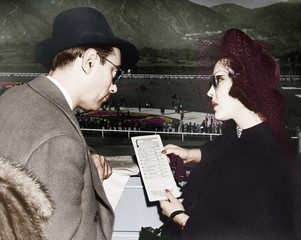 Elegant couple at a horse race looking at a program  