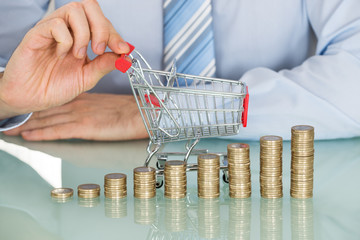 Businessman With Stacked Coins And Small Shopping Cart
