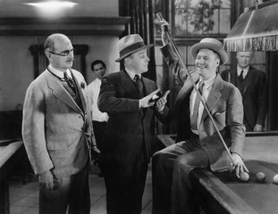 Two men talking to each other and a man standing beside them at a pool place 