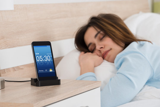 Woman Sleeping On Bed With Alarm On Mobile Phone