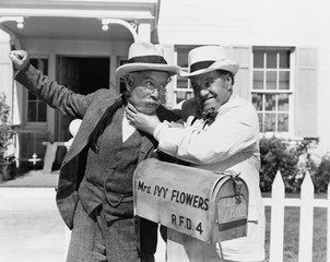 Two mature men fighting near a mail box in front of a house 