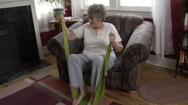 Elderly woman doing exercise with elastic bands at home.