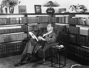 Man sitting in his library reading a book 