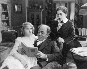 Father reading to his daughter while his son is sneaking up from behind 