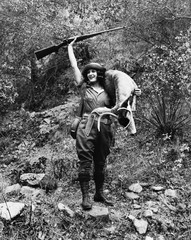 Oh deer, a young female hunter with gun raised high smiles with a young buck in hand 
