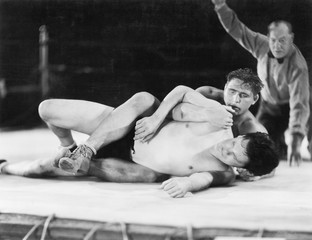 Two men wrestling with a referee in the background 