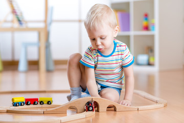Child boy playing with wooden railway on the floor