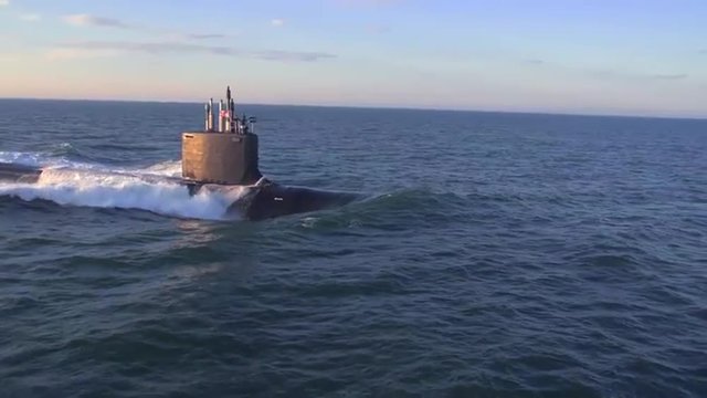 Excellent aerials over a submarine at sea with dolphins jumping across bow.