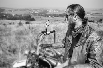Portrait of biker with long hair and beard in a leather jacket and sunglasses sitting on his bike...