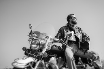 Portrait of a young man with beard sitting on his cruiser motorcycle. Man is wearing leather jacket...