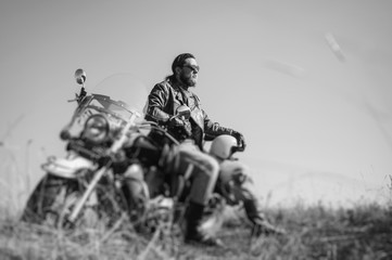 Portrait of a young happy biker with beard sitting on his cruiser motorcycle. Man is wearing...