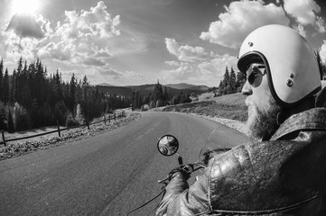 Young man biker driving on the open road in the mountains, wearing leather jacket and helmet. Shot...