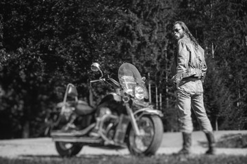 Handsome man with long hair and beard standing near his motorcycle. Biker is wearing leather jacket...