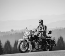 Brutal biker with beard in sunglasses, jeans and a leather jacket sitting on the travel motorbike....