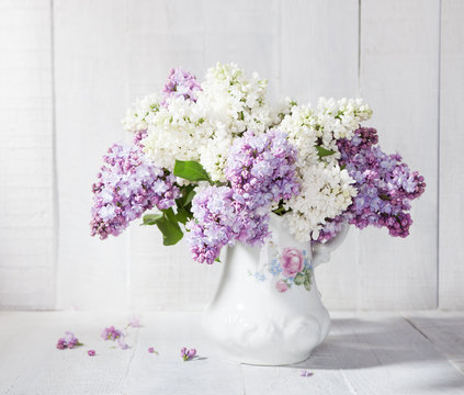 Lilac bouquet in ceramic jug against a white wooden wal