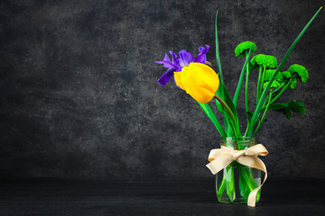 beautiful iris with tulip and green chrysanthemums in a jar with water on a dark wooden table the dark background