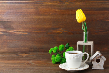 beautiful yellow Tulip in a vase near a Cup of coffee and green chrysanthemums on a brown wooden background