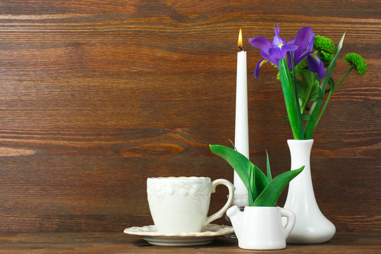 beautiful iris with green chrysanthemums in a vase near the candle with a Cup of coffee on brown wooden background