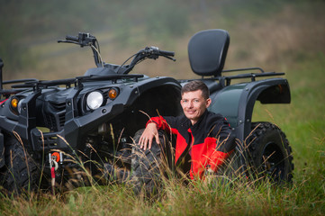 Young man sitting near four-wheeler ATV. Smiling and looking to the camera