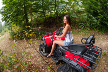 Fototapeta na wymiar Beautiful girl driving four-wheeler ATV. Smiling and looking towards the camera. View from the back