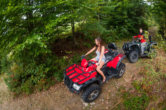 Happy beautiful couple driving four-wheelers ATV. Girl is leading the way