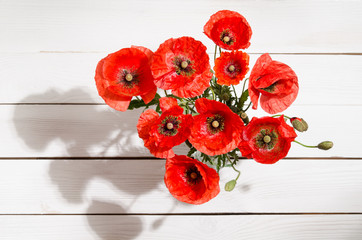 Bouquet of red poppies in glass vase on old white wooden table