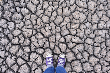 Human legs in sneakers and jeans standing on dried cracked earth