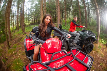 Happy beautiful couple driving four-wheelers ATV. Lady is looking at the camera
