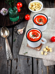 Tomato cream soup in mugs and greens on a wooden table.
