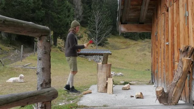 Man chopping wood in the forest with an axe wearing traditional austrian clothes