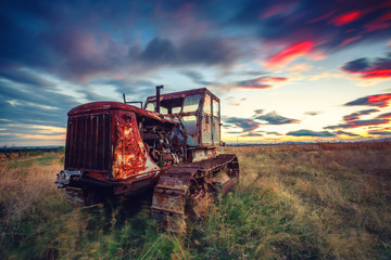 Beautiful sunset over field and old rusty tractor