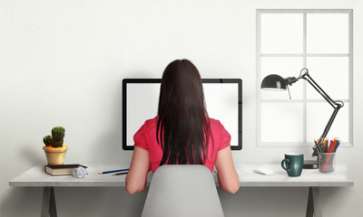 Woman work on office computer with isolated screen for mockup. Modern office interior with window, lamp, plant, coffee, pencils.