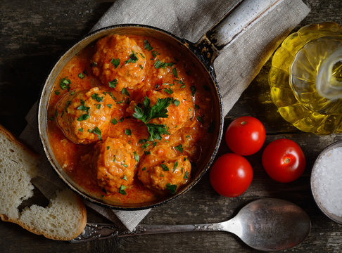 meatballs in tomato sauce in the pan, bread and tomato on a wooden background