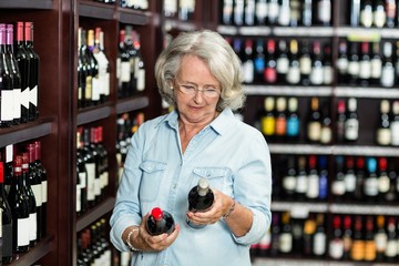 Smiling senior woman choosing wine at the supermarket