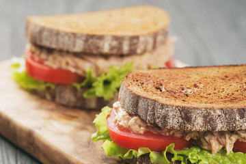 rye bread sandwich with tuna and vegetables on wood background