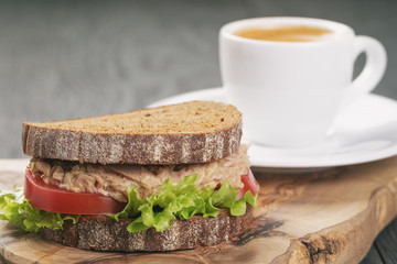 rye bread sandwich with tuna and coffee on wood background