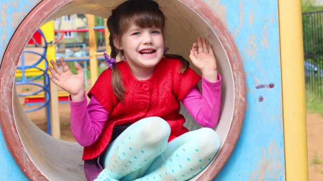 Little beautiful girl sitting in tube on playground