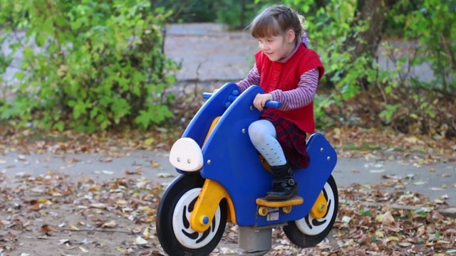Little girl in red vest on wooden motorbike playing on playground