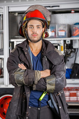 Fototapeta premium Serious Firefighter Standing Arms Crossed Against Firetruck