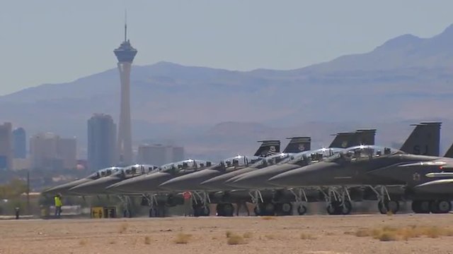 Numerous F-15 and F-16 fighter jets line up and taxi for takeoff in a military exercise.