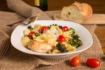 Authentic Italian meal with homemade orecchiette pasta, chicken, broccoli, tomatoes. Loaf of Italian bread and bottle of wine in the background